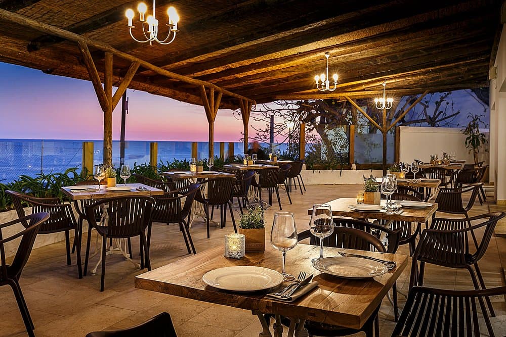 Terraza de restaurante frente al mar en Barbate, Cádiz, con mesas puestas para cenar al atardecer